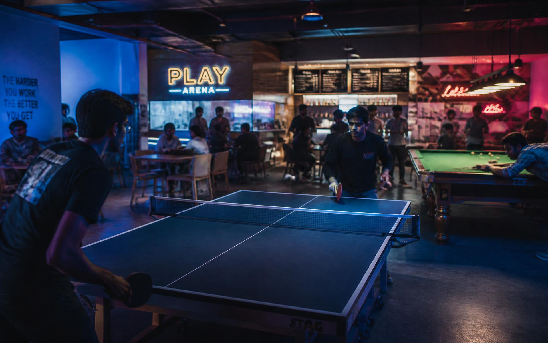 Young people playing table tennis and snooker inside Mini Arena's lit lounge